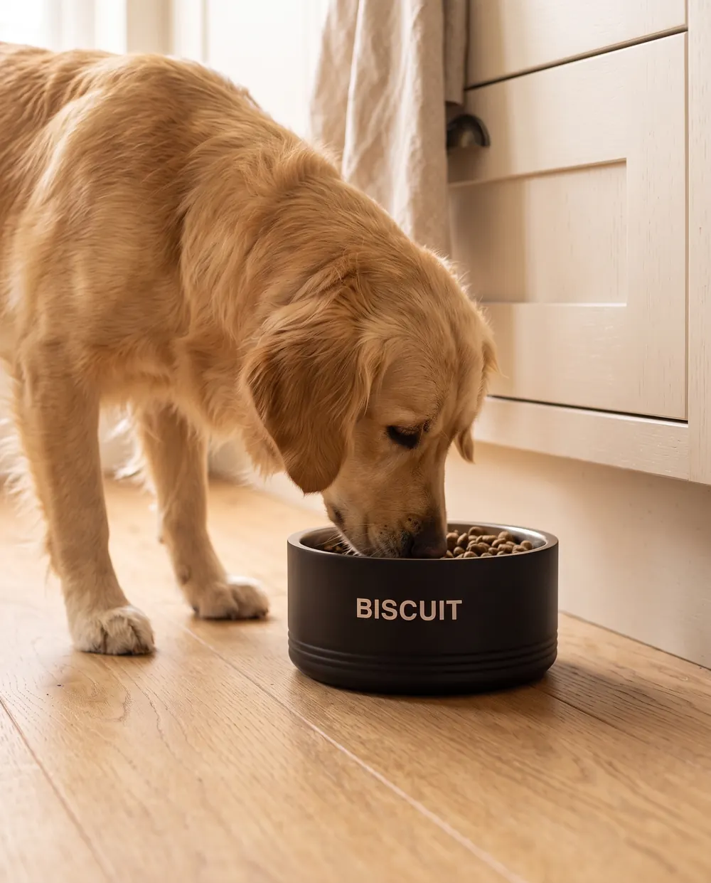 A golden retriever eating from the black steel bowl, its name on the side, on a kitchen floor